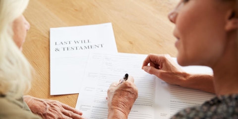 Female Friend Helping Senior Woman To Complete Last Will And Testament At Home